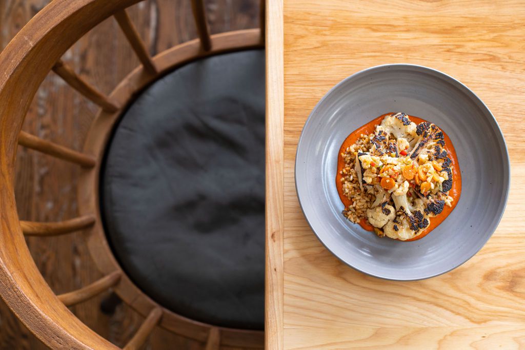 A colorful cauliflower dish sits inside a gray bowl on a light wood table.