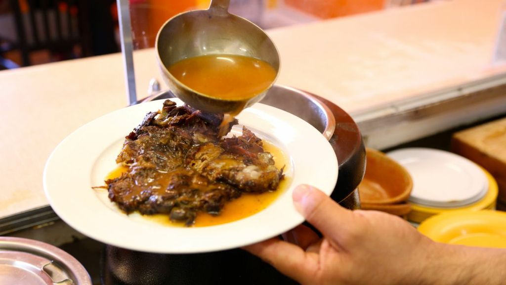 A server pours juices over a plate of goat meat.
