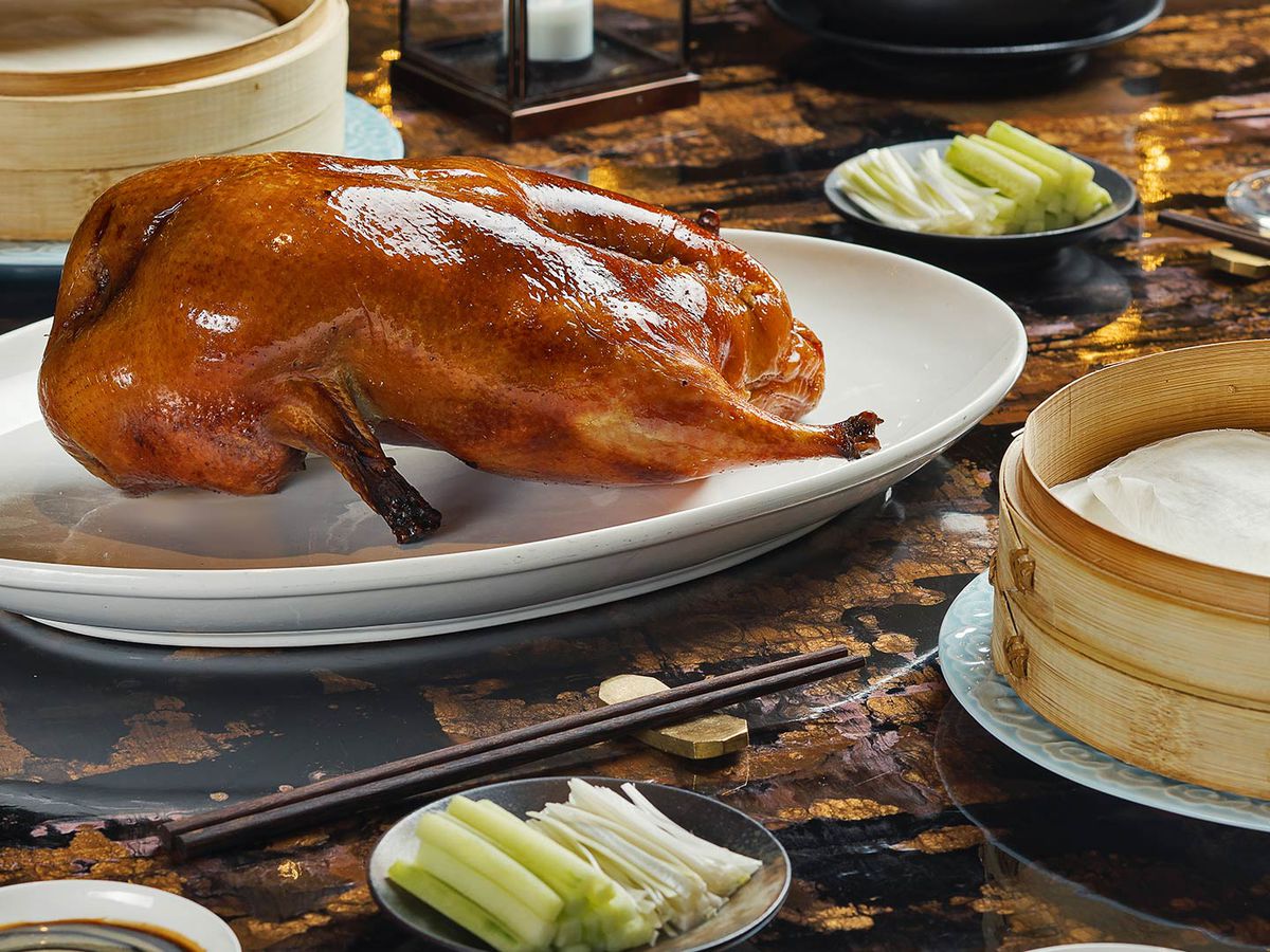A whole roasted duck on a white plate with bamboo steamers on either side.