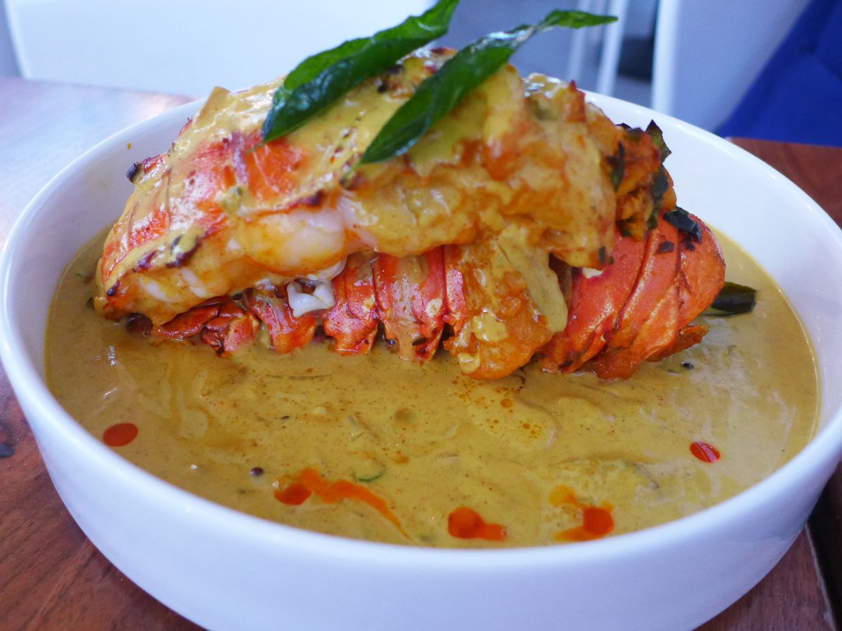 The image showcases a lobster tail, immersed in a thick gravy, resting on top of its own removed shell.