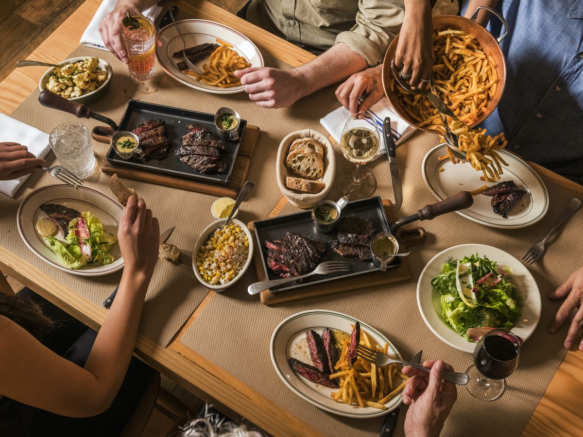Witness a captivating aerial shot featuring four guests savoring skirt steak alongside an array of delectable sides.