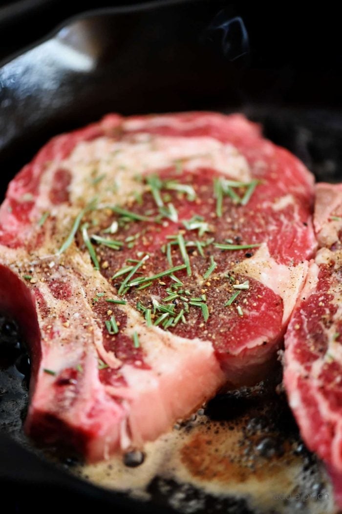 Rib eye Steak sprinkled with seasoning and rosemary cooking in butter in an iron skillet. // addapinch.com